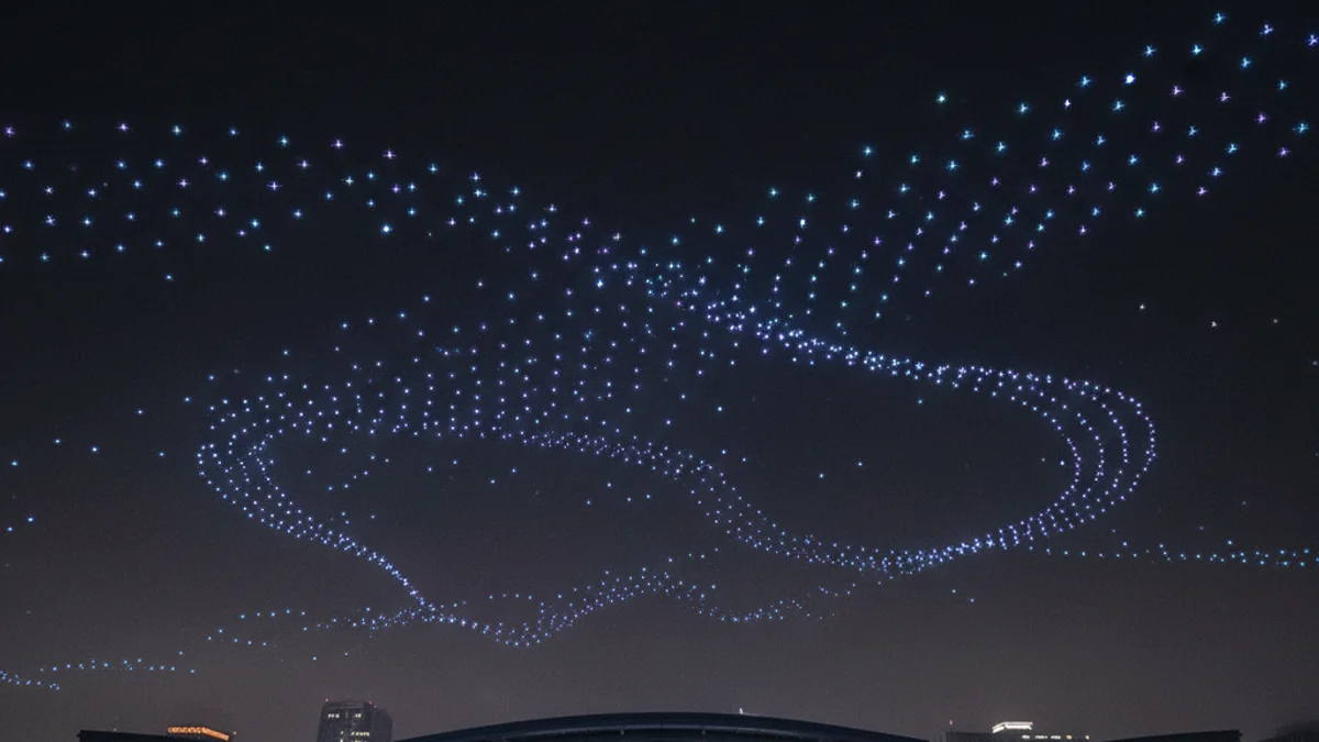 Espectáculo nocturno de drones iluminados sobre un recinto ferial, creando figuras de luz en el cielo.