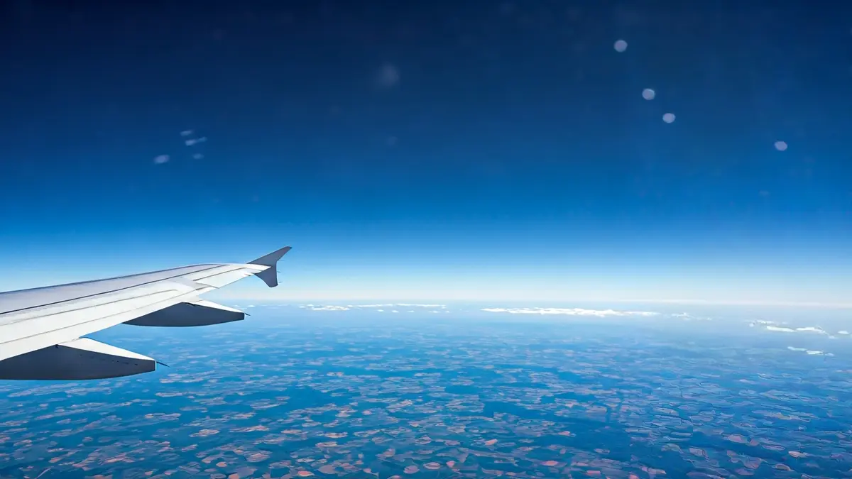 Imagen genérica de un ala de avión en vuelo, con nubes y tierra al fondo.