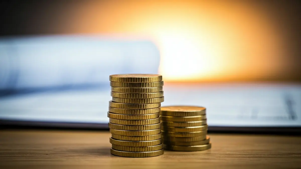 Imagen genérica de monedas de euro sobre una mesa, con planos arquitectónicos desenfocados al fondo.