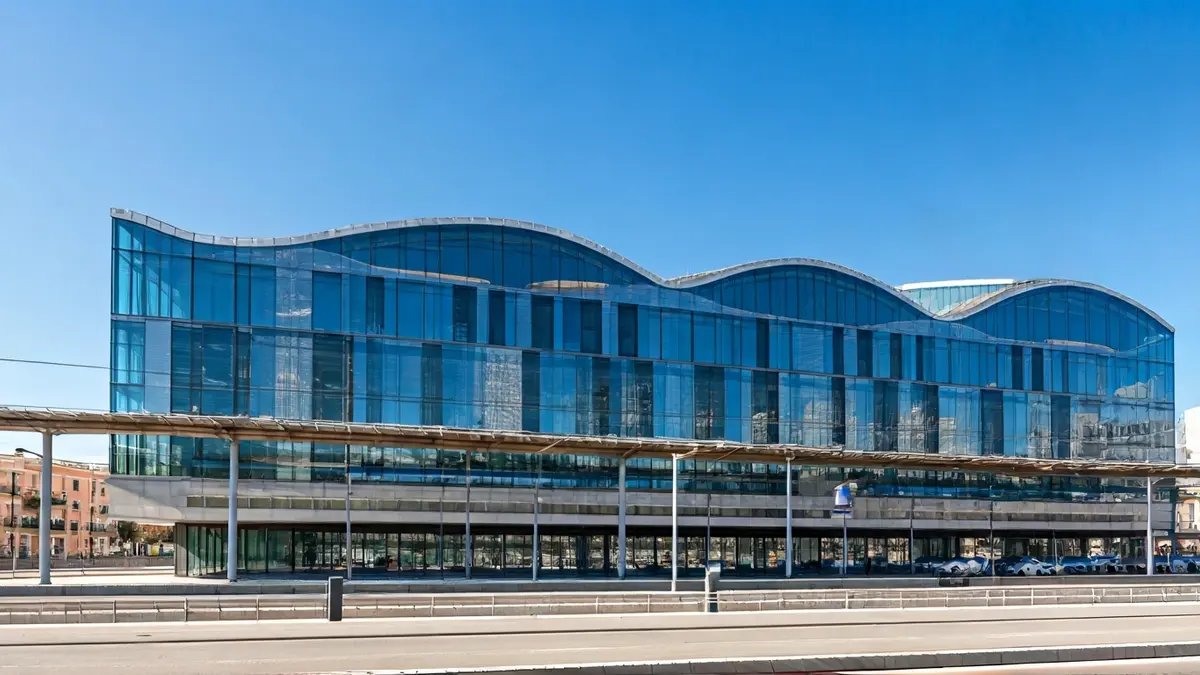 Imagen de un edificio moderno y vanguardista, con grandes ventanales, cerca de una estación de tren.