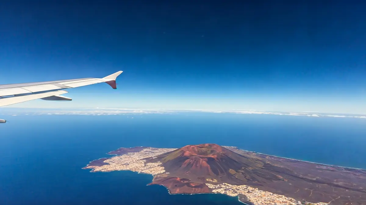 Image of an airplane wing flying over a volcanic landscape in Canarias.