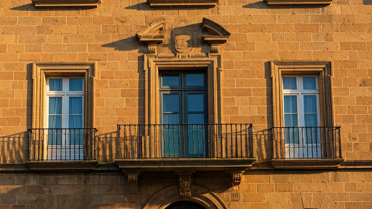Fachada del ayuntamiento de Novelda con balcones de hierro forjado y luz solar cálida.