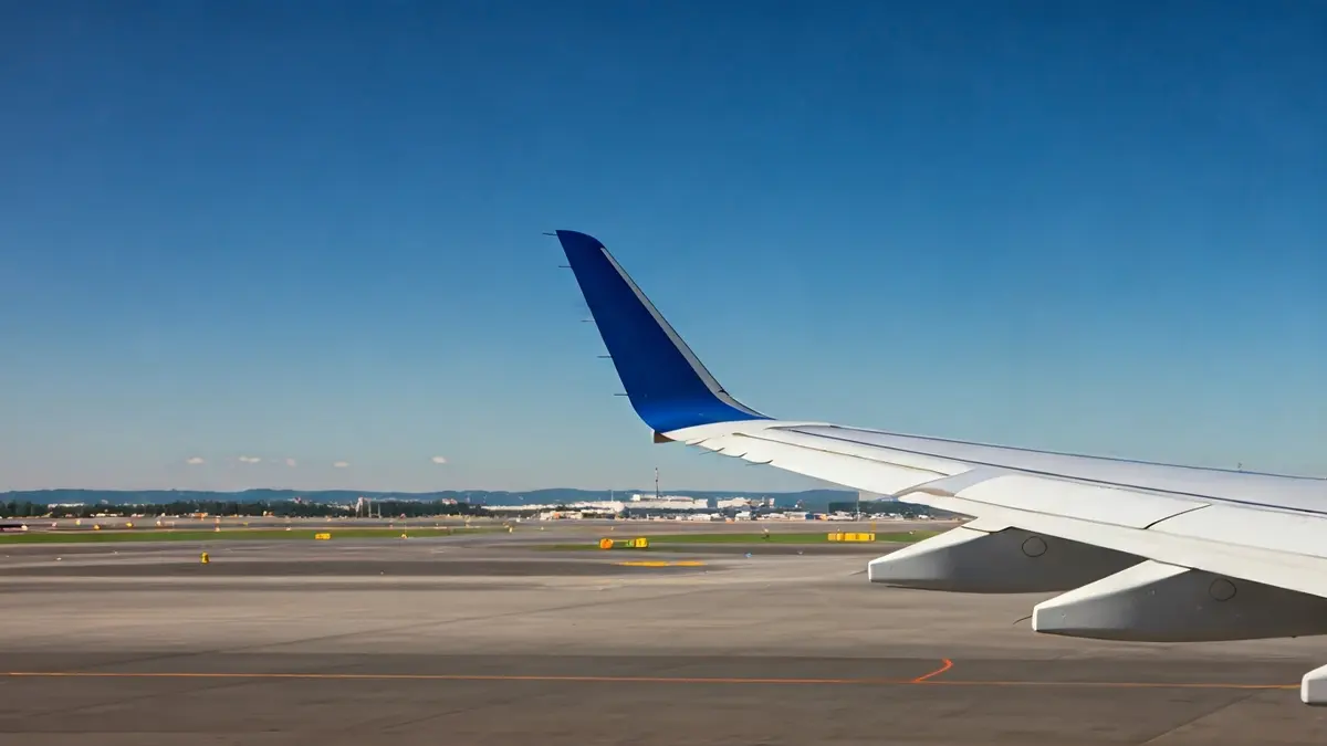 Imagen genérica de un ala de avión en el cielo, con luces de pista borrosas al fondo.