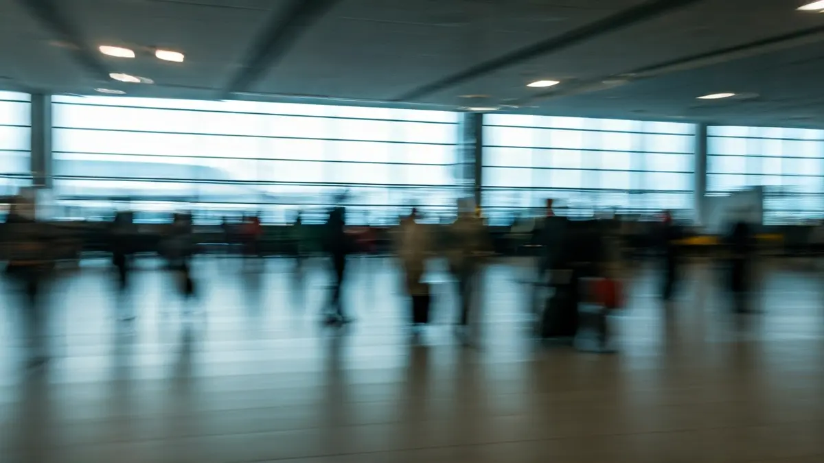 Imaxe xenérica dunha terminal de aeroporto con pasaxeiros e avións ao fondo.