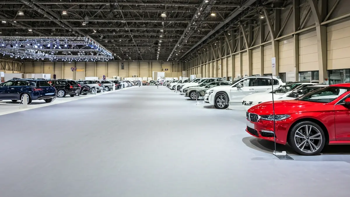 Imaxe xenérica dun salón de exposicións de vehículos baleiro, con coches modernos en ringleira e carteis de 'en venda'.