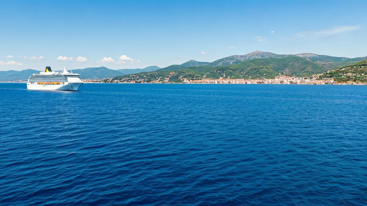 Imagen genérica de un crucero navegando por aguas azules con la costa mediterránea al fondo.