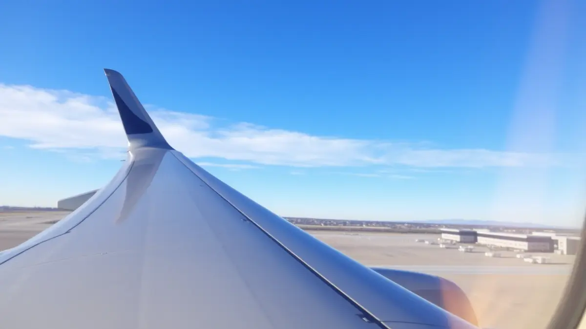 Imagen genérica de un ala de avión contra un cielo azul, con pista de aterrizaje y terminal difuminadas al fondo.