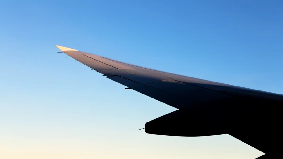 Silhouette of an airplane wing against a blue sky.