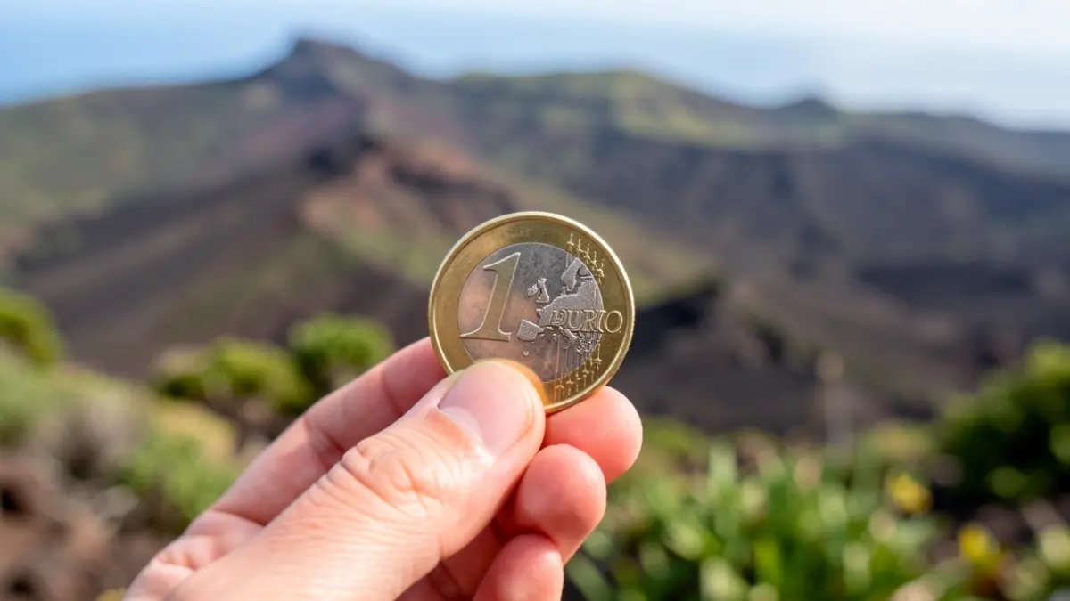 Close-up of a hand holding a euro coin with a Canary Islands landscape in the background.