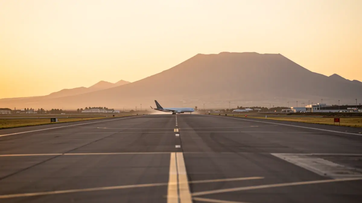Imagen de una pista de aterrizaje al atardecer con silueta de avión al fondo.