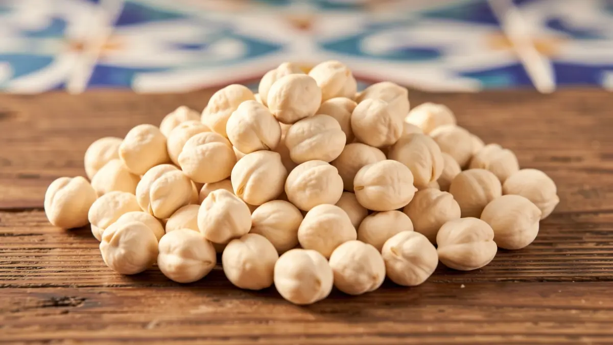 Garbanzos de la variedad 'blanco lechoso' de la Campiña de Córdoba sobre una superficie de madera rústica con detalles de azulejo andaluz.