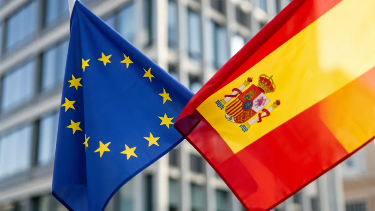 Banderes d'Espanya i la Unió Europea entremesclades davant un edifici d'oficines modern.