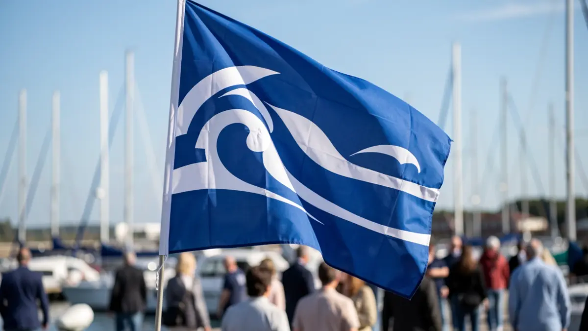 Imagen de una bandera náutica azul y blanca con un diseño de ola, en un muelle con barcos.