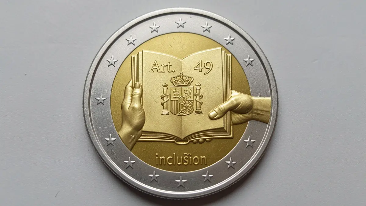 Primer plano de una moneda conmemorativa de 2 euros con el artículo 49 de la Constitución y el escudo de España.