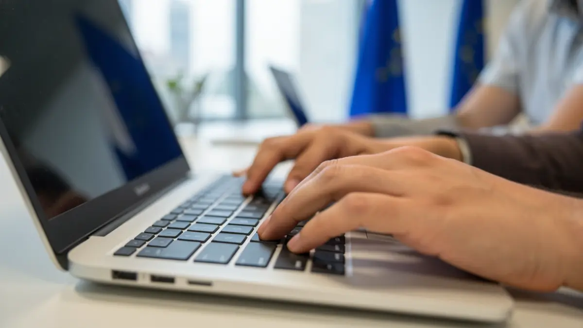 Imagen genérica de manos diversas escribiendo en un teclado de portátil en una oficina moderna con motivos de la Unión Europea.